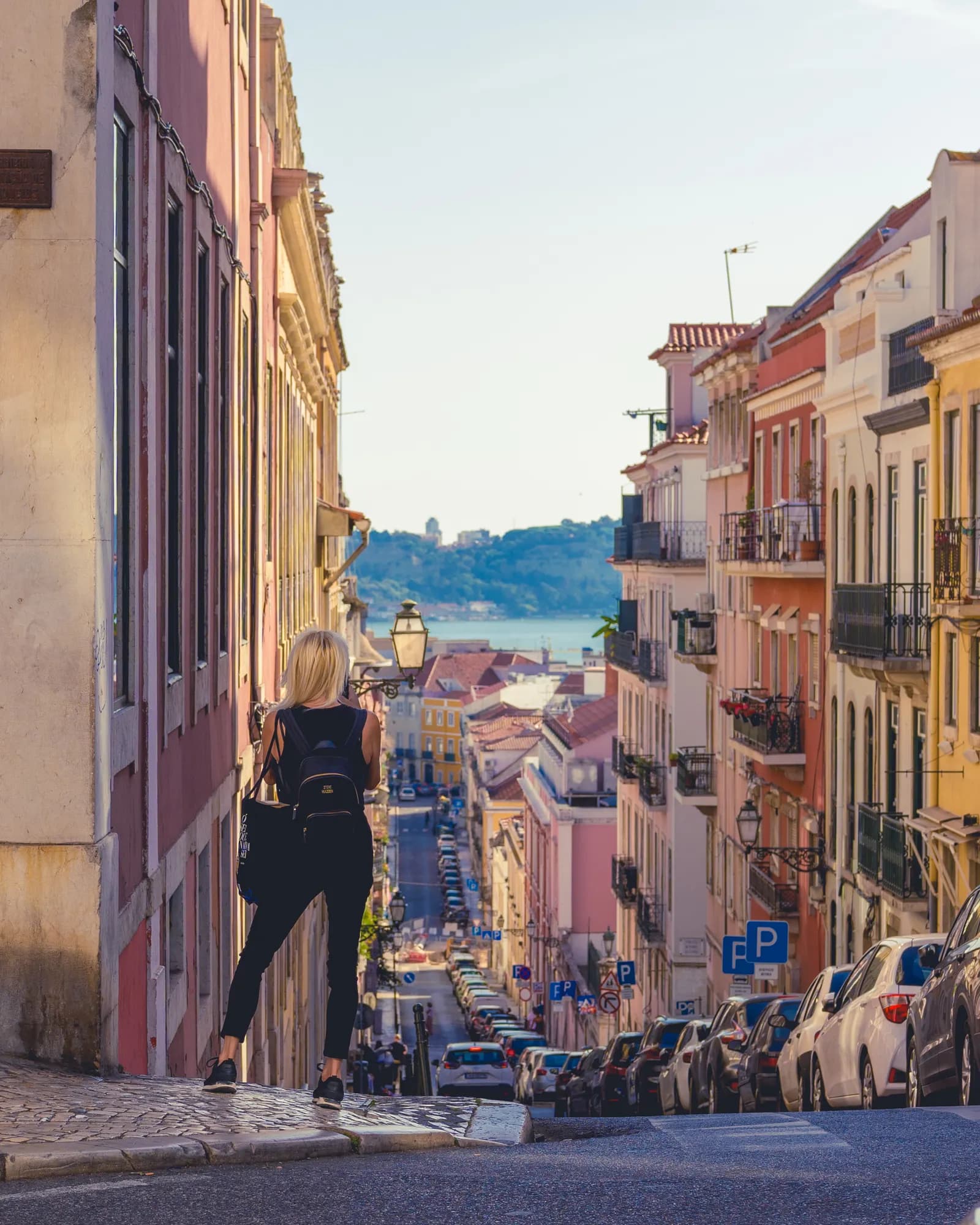 Woman with a backpack looking across a Lisbon street at sunset